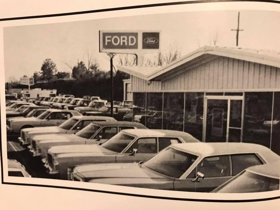 Ford dealership lot with rows of cars and a Ford sign
